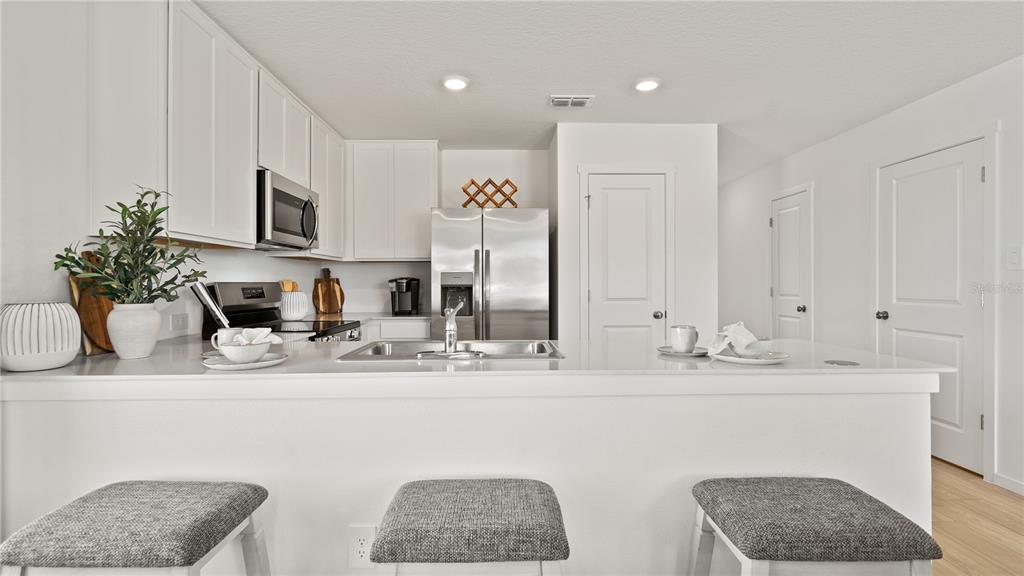 A modern kitchen features white cabinets, stainless steel appliances, and a breakfast bar with stools — 1553 PLANK PLACE, DAVENPORT, FL