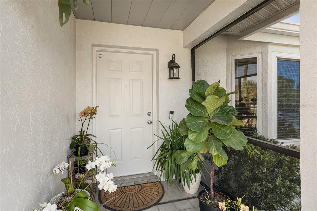 A white front door sits on a covered porch with potted plants and a mat — 2600 PALMETTO STREET, NOKOMIS, FL