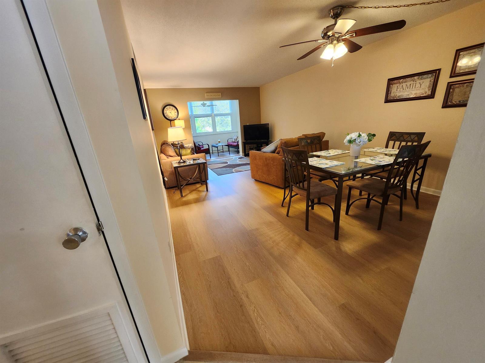 An open-concept living and dining area features wood-look flooring, a ceiling fan, and furniture — 2600 NE 1st Lane # 311, Boynton Beach FL 33435, BOYNTON BEACH, FL