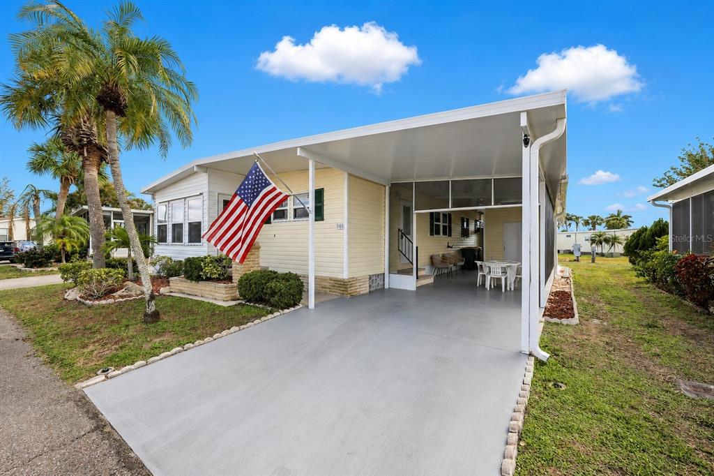 A light yellow mobile home features a large carport, a front porch, and an American flag — 2100 KINGS HIGHWAY UNIT 840, PORT CHARLOTTE, FL