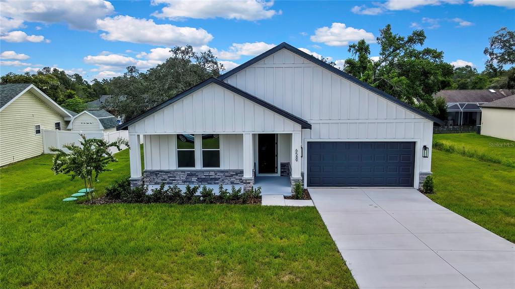 A single-story house with white vertical siding, a stone base, and a dark garage door — 6589 FREEPORT DRIVE, SPRING HILL, FL