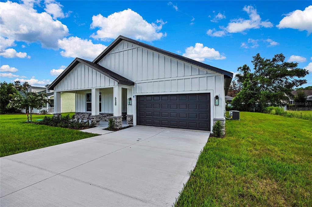 A white farmhouse-style house features a dark garage door, stone accents, and a concrete driveway — 6589 FREEPORT DRIVE, SPRING HILL, FL