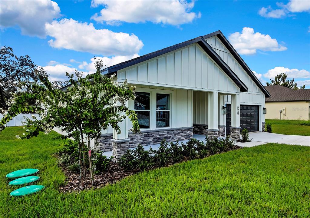 A single-story house with white vertical siding, stone accents, and a dark garage door — 6589 FREEPORT DRIVE, SPRING HILL, FL