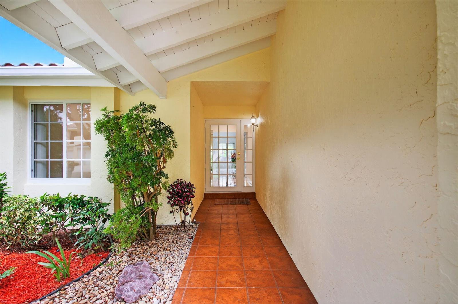 A covered entryway features a tiled walkway, a glass-paneled front door, and a landscaped garden — 6105 Via Laguna Lane, Boca Raton FL 33433, BOCA RATON, FL