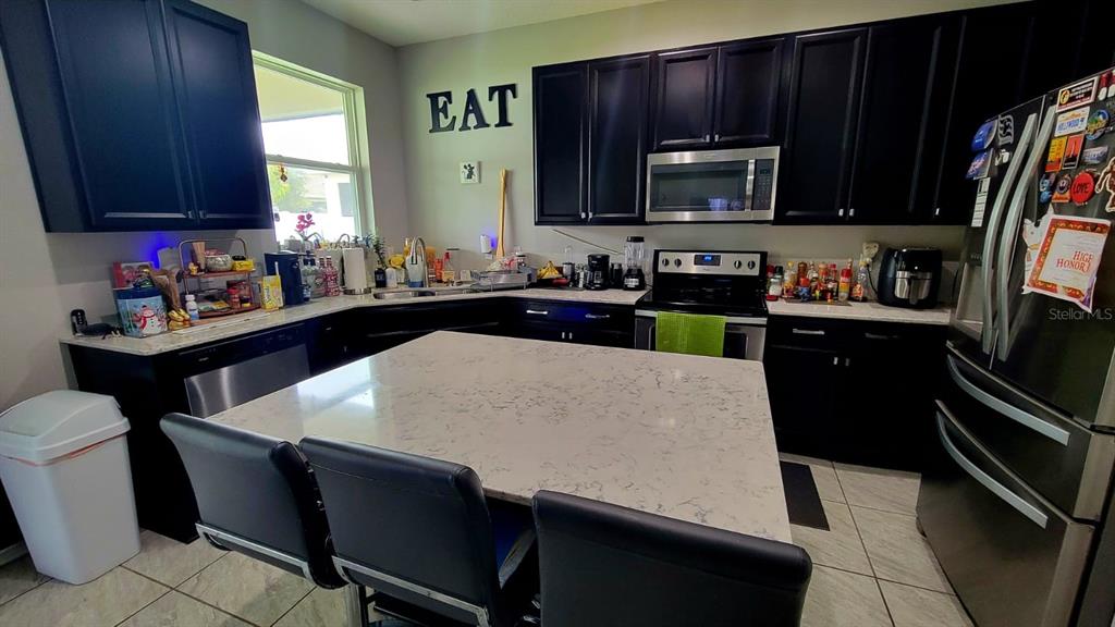 A kitchen features dark cabinets, a large quartz-topped island, and stainless steel appliances — 12372 STONE BARK TRAIL, ORLANDO, FL