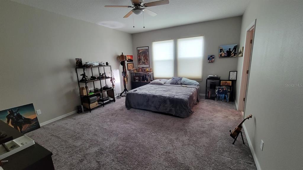 A bedroom with gray carpet, a bed, a ceiling fan, and shelving units — 12372 STONE BARK TRAIL, ORLANDO, FL