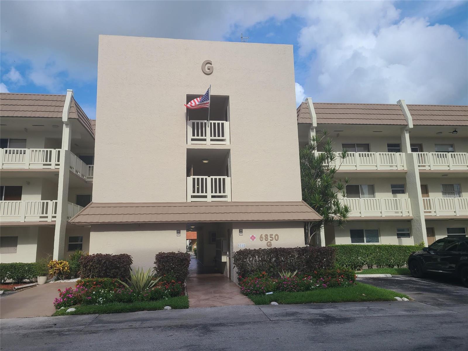 A three-story apartment building exterior with a tan facade, balconies, and a central walkway — 6850 Royal Palm Boulevard # 212, Margate FL 33063, MARGATE, FL