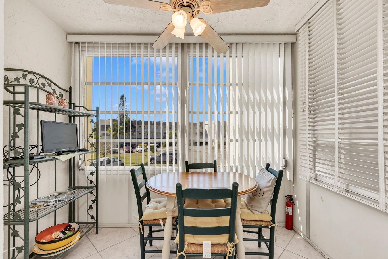 A sunroom features a round dining table with four chairs, a metal shelving unit, and blinds — 6850 Royal Palm Boulevard # 212, Margate FL 33063, MARGATE, FL