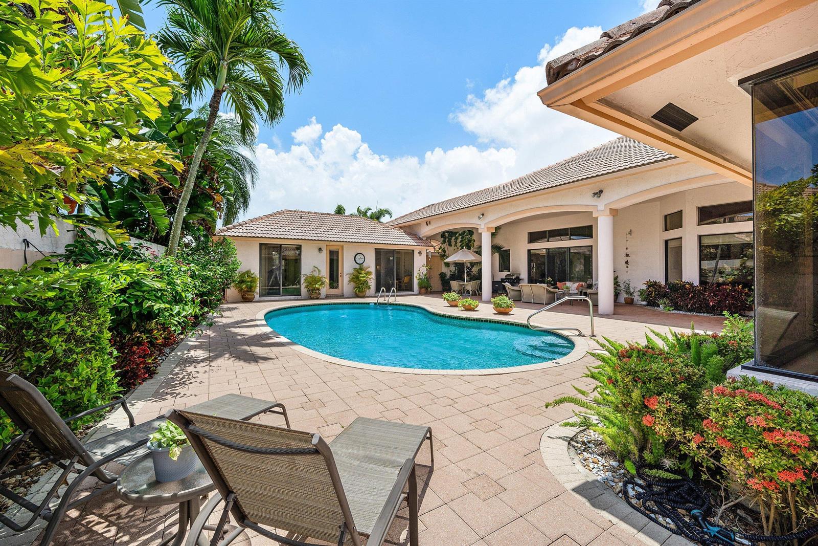 A backyard patio features a kidney-shaped swimming pool, lounge chairs, and lush tropical landscaping — 4727 Bocaire Boulevard, Boca Raton FL 33487, BOCA RATON, FL