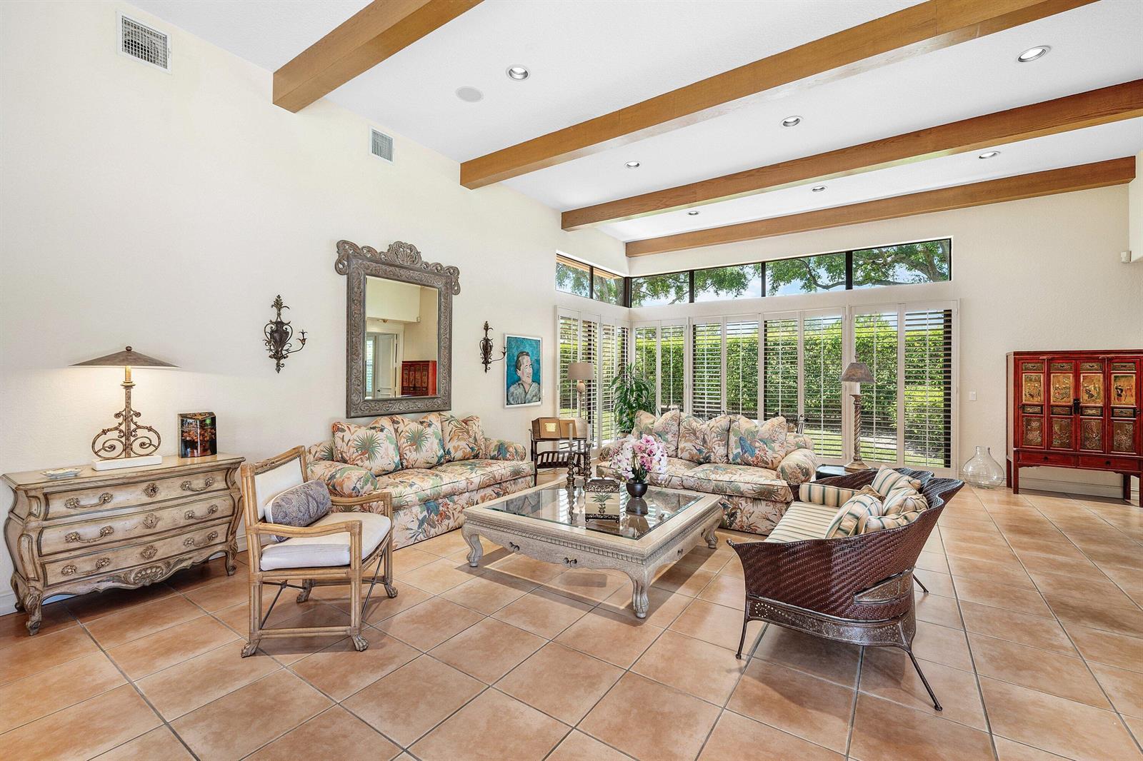 A spacious living room features vaulted ceilings with exposed wood beams, tile flooring, and large windows — 4727 Bocaire Boulevard, Boca Raton FL 33487, BOCA RATON, FL