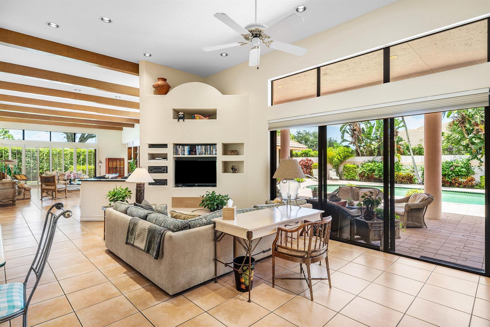 A living room features a beige sectional, a desk, exposed ceiling beams, and sliding glass doors — 4727 Bocaire Boulevard, Boca Raton FL 33487, BOCA RATON, FL