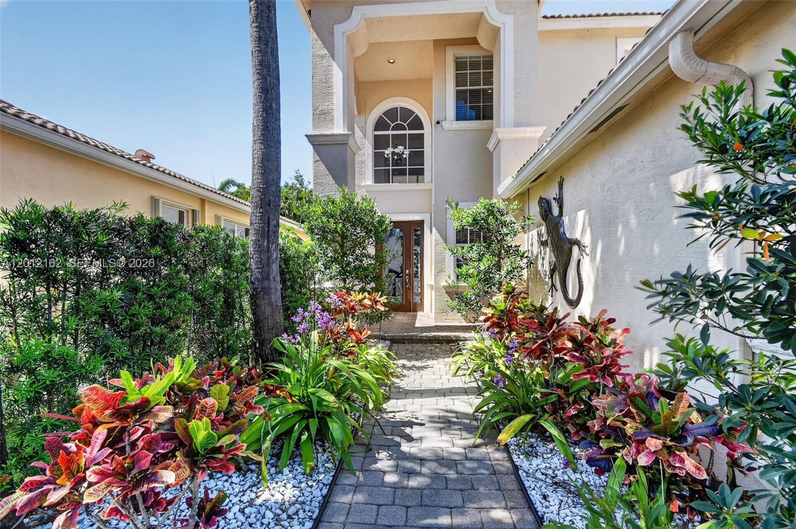 A stone walkway leads to the front entrance of a two-story house with landscaping — 7055 Via Leonardo, Lake Worth FL 33467, LAKE WORTH, FL