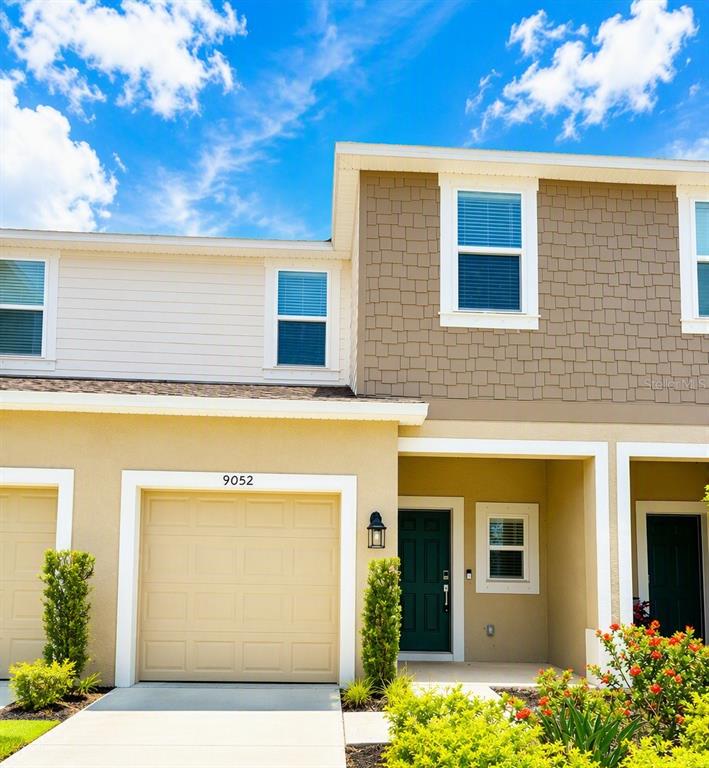 The exterior of a two-story townhouse features a tan garage, a dark green door, and siding — 9052 DRIVEN SNOW STREET, SARASOTA, FL