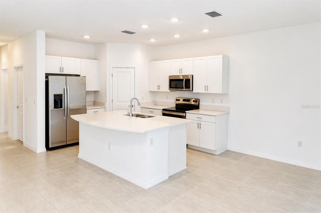 A modern kitchen features white cabinets, stainless steel appliances, and a central island with seating — 9052 DRIVEN SNOW STREET, SARASOTA, FL