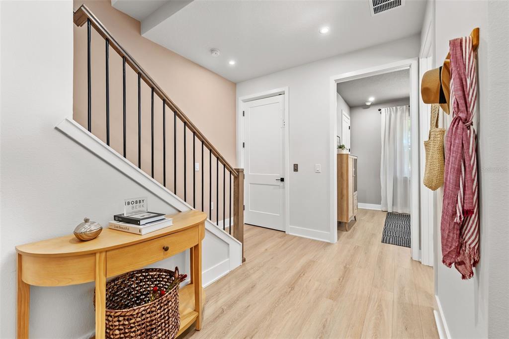 A light-filled entryway features a wooden console table, a staircase, and a doorway to another room — 2111 TIDEWATCH LOOP, NEW SMYRNA BEACH, FL