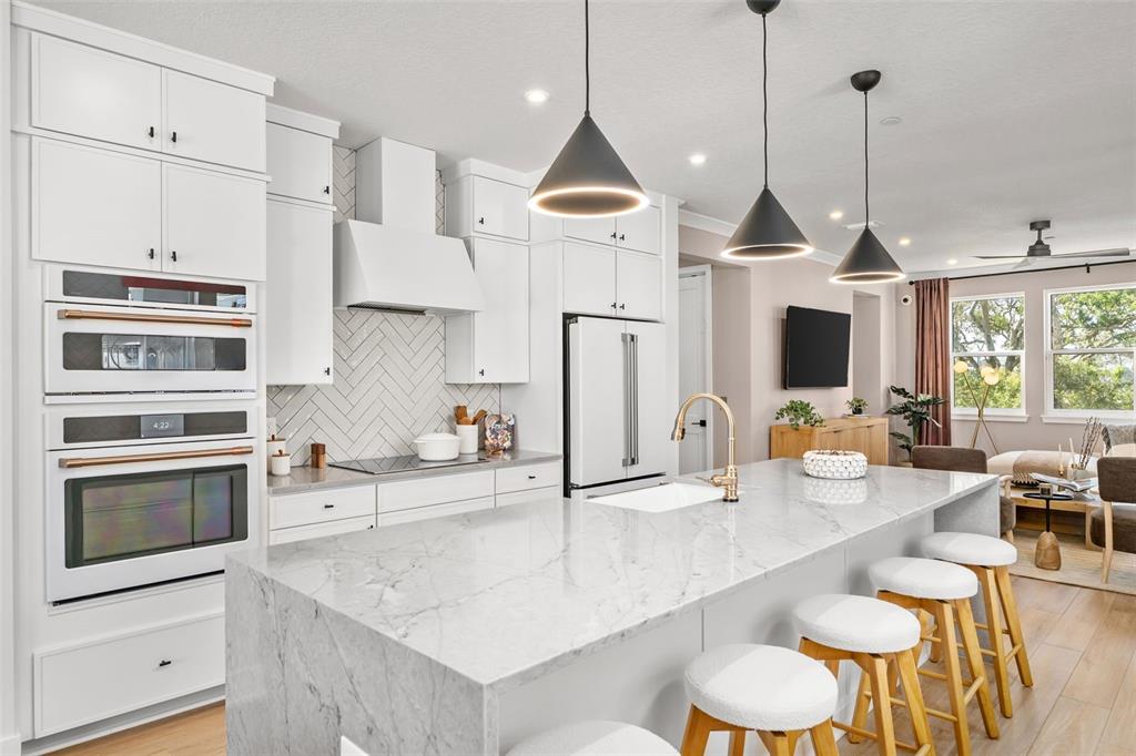 A modern kitchen features white cabinetry, a marble-topped island, and three black pendant lights — 2111 TIDEWATCH LOOP, NEW SMYRNA BEACH, FL