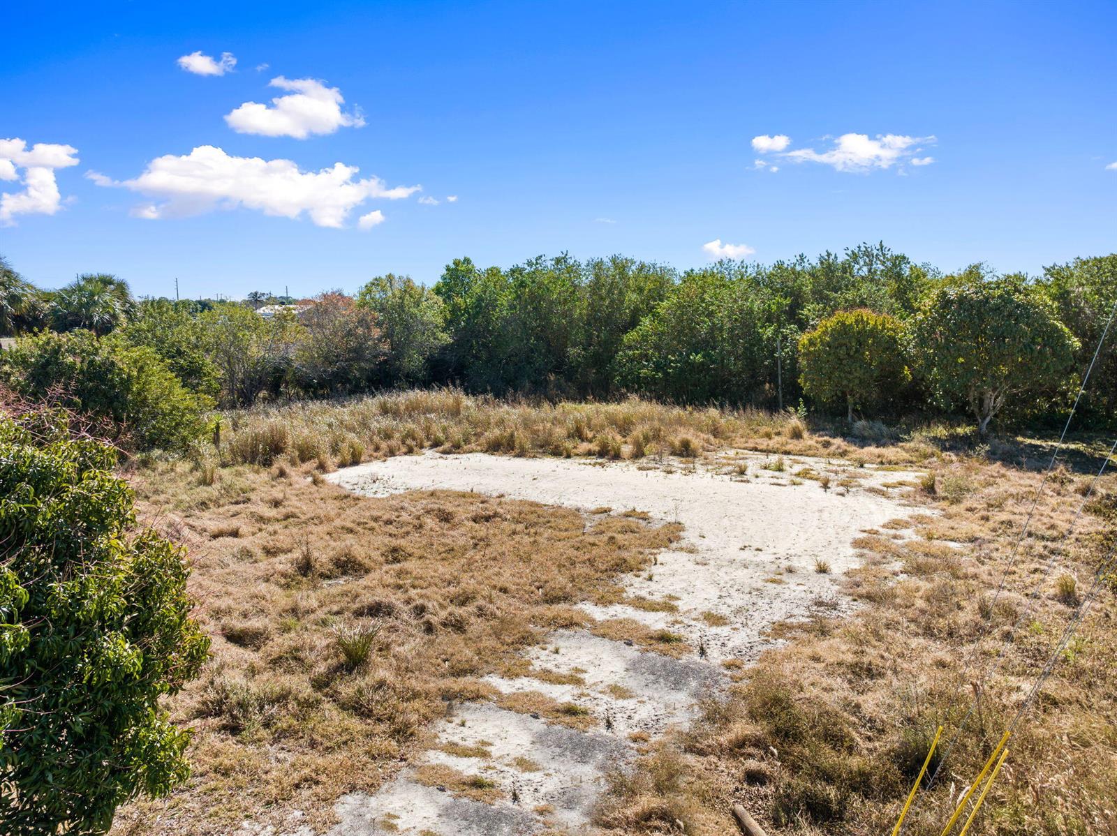 An elevated view of a sandy, grass-covered vacant lot bordered by dense green trees — 6406 Oleander Avenue, Fort Pierce FL 34982, FORT PIERCE, FL