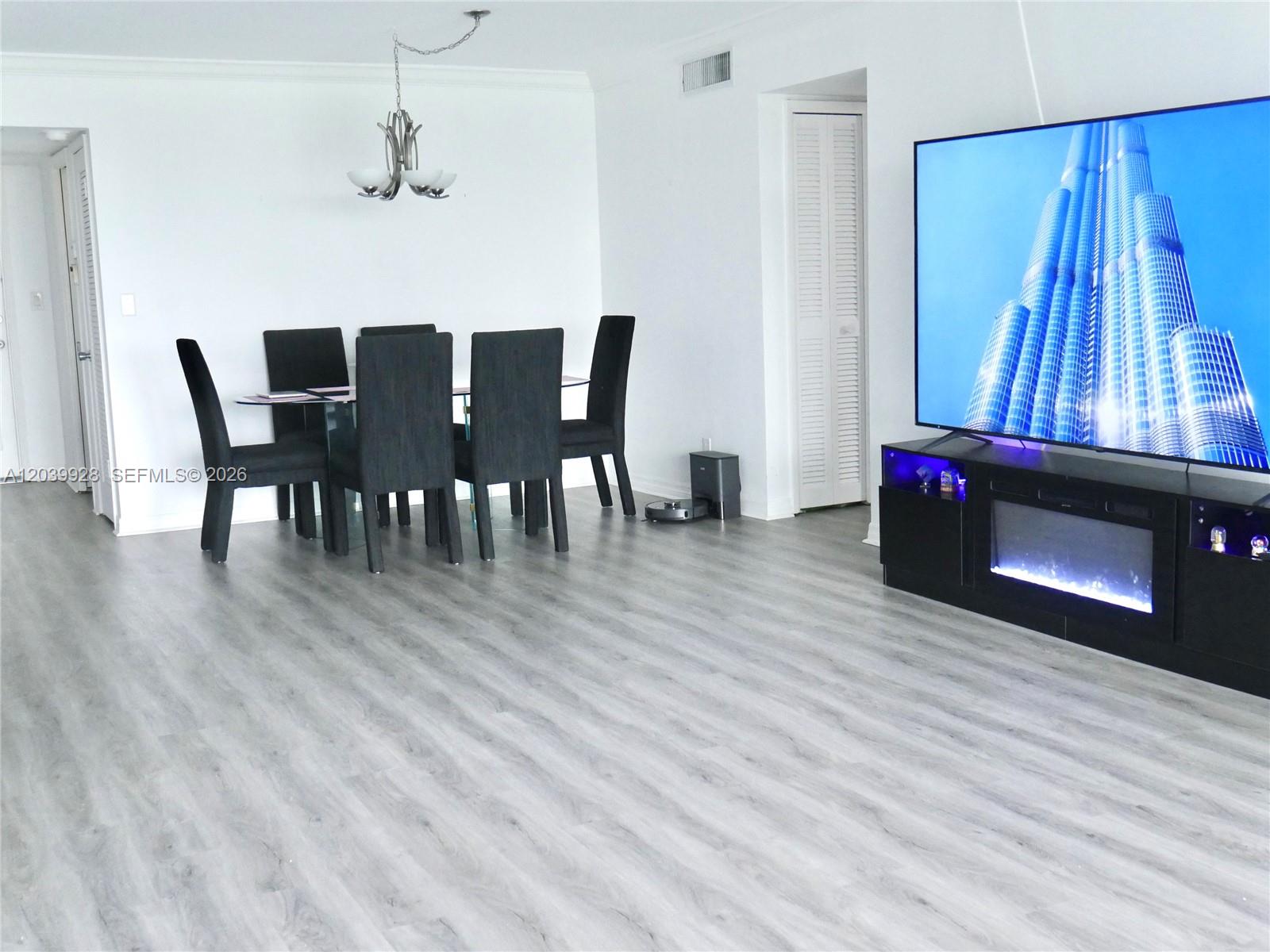 A dining area and living space feature gray wood-look flooring and a large television — 3001 S Course Dr # 508, Pompano Beach FL 33069, POMPANO BEACH, FL