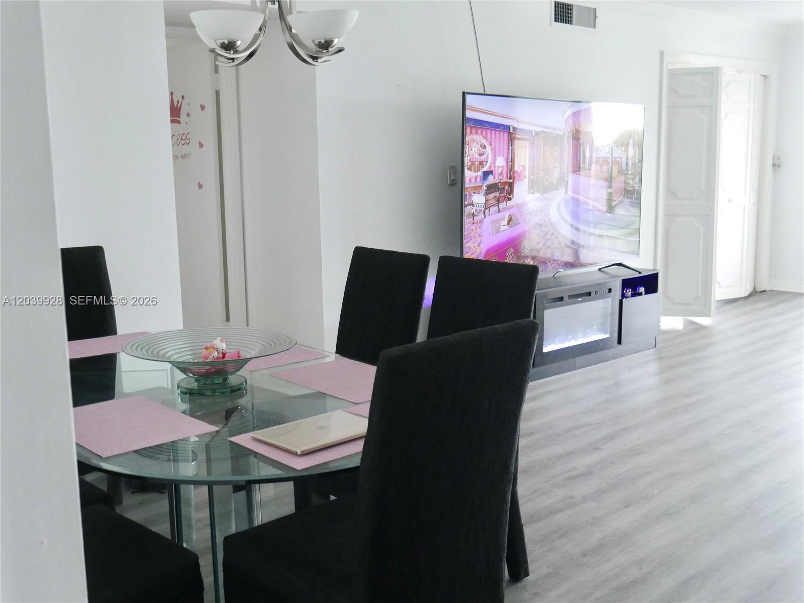 A dining area with a glass table and black chairs sits near a television console — 3001 S Course Dr # 508, Pompano Beach FL 33069, POMPANO BEACH, FL