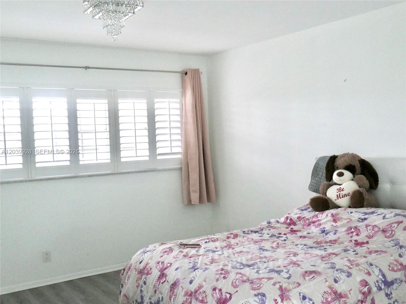 A bedroom features a bed with a butterfly-patterned comforter, white shutters, and a crystal chandelier — 3001 S Course Dr # 508, Pompano Beach FL 33069, POMPANO BEACH, FL