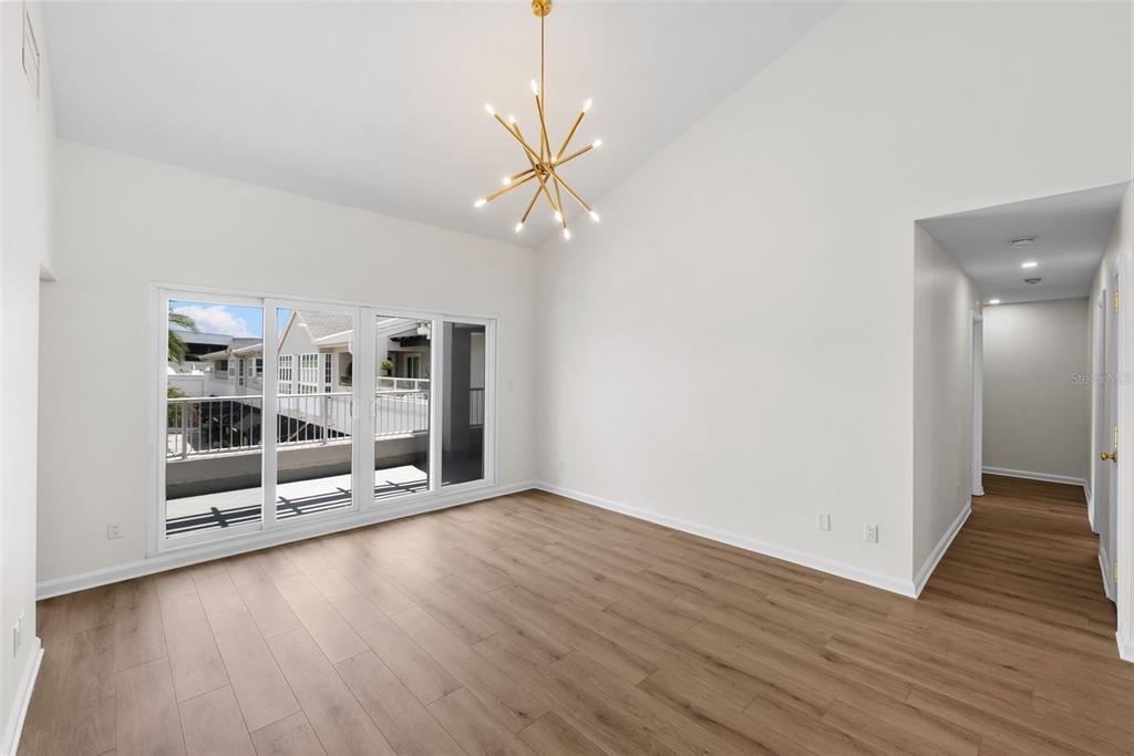 An empty room with light wood floors, white walls, a modern chandelier, and sliding glass doors — 1647 W SNOW CIRCLE UNIT 204, TAMPA, FL