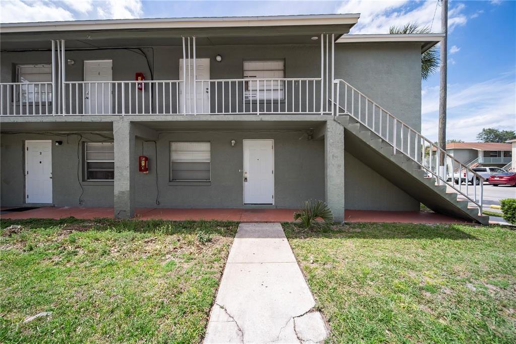 A two-story apartment building exterior features white doors, a concrete walkway, and an outdoor staircase — 702 MICHIGAN COURT UNIT 1, ST CLOUD, FL