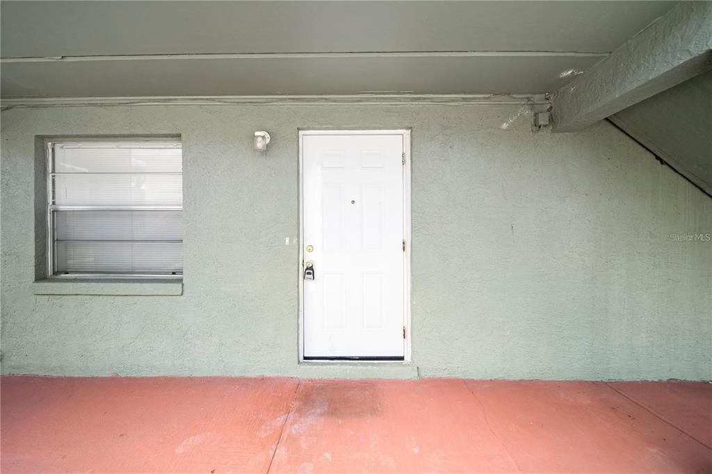 A white door and a window are set into a light green stucco exterior wall — 702 MICHIGAN COURT UNIT 1, ST CLOUD, FL