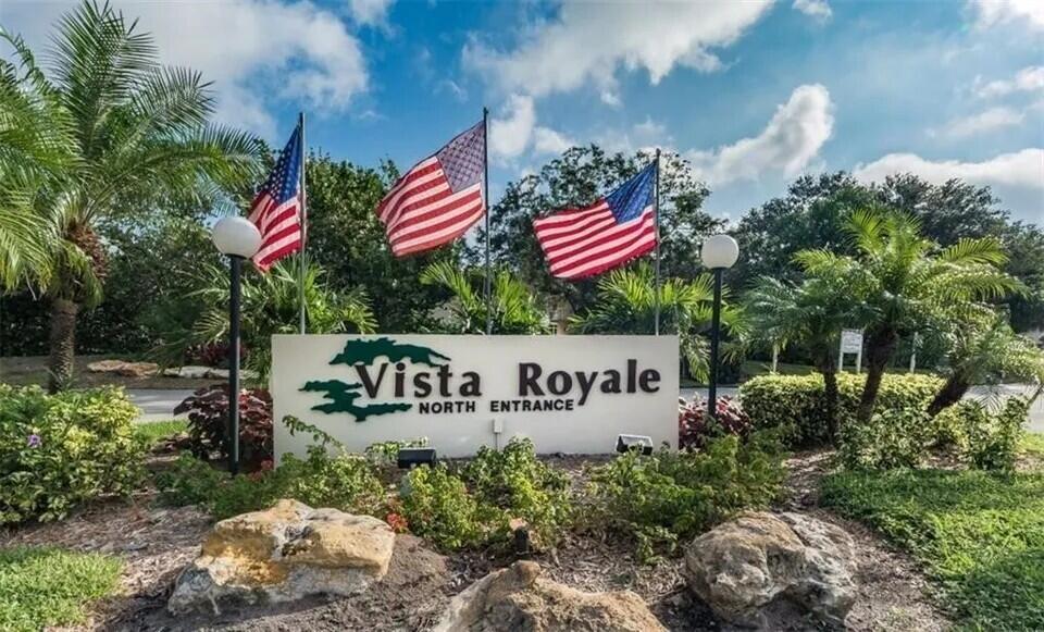 A sign for Vista Royale North Entrance stands outdoors with three American flags behind it — 98 Spring Lake Drive # 103, Vero Beach FL 32962, VERO BEACH, FL