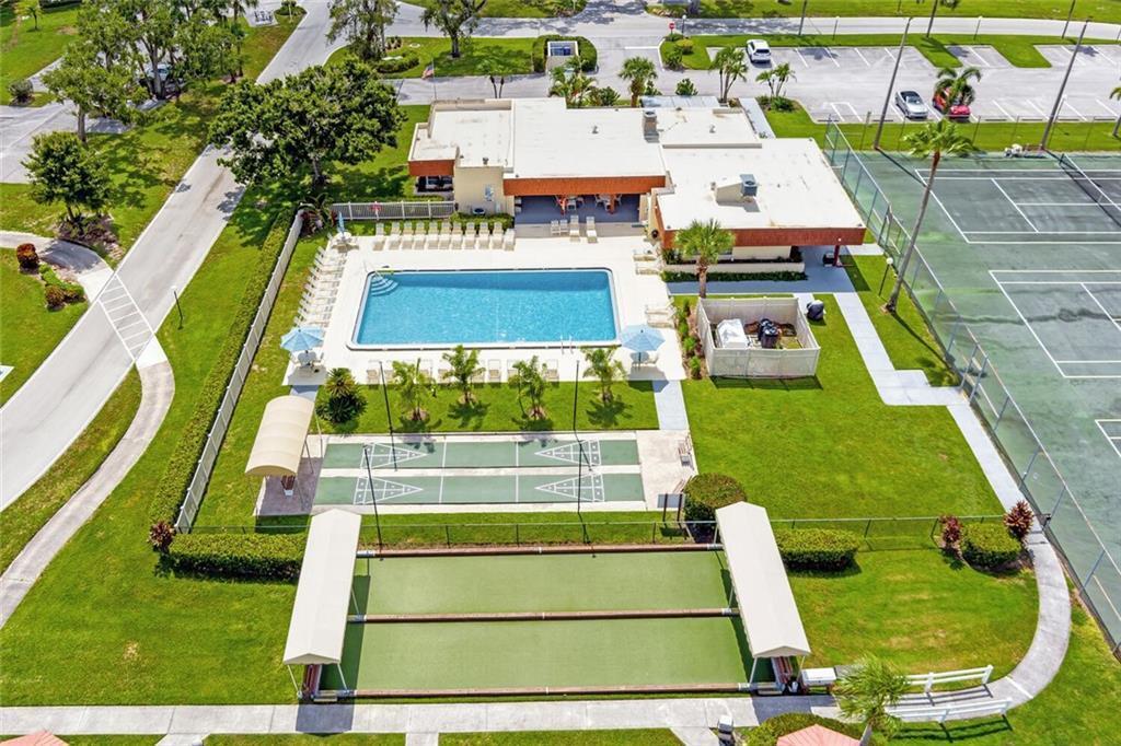 An aerial view shows a swimming pool, tennis courts, and shuffleboard courts at a community center — 98 Spring Lake Drive # 103, Vero Beach FL 32962, VERO BEACH, FL
