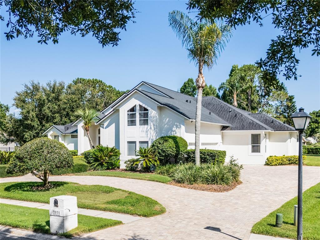 A white house with a dark roof and a paved driveway sits behind a lawn — 2031 WILLOW LAUREN LANE UNIT L, WINDERMERE, FL