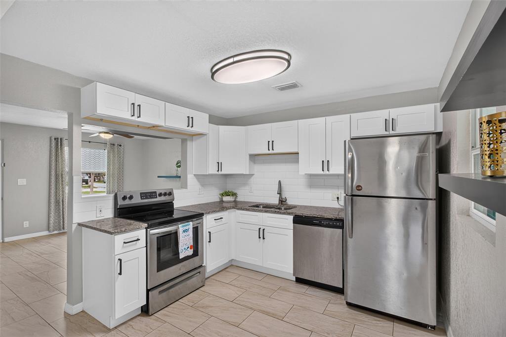 A kitchen with white cabinets, stainless steel appliances, granite countertops, and light-colored tile flooring — 4529 73RD STREET N, ST PETERSBURG, FL