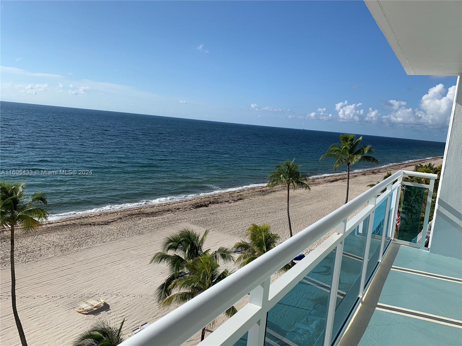 A high-angle view from a balcony overlooking a sandy beach, palm trees, and the ocean — FORT LAUDERDALE, FL