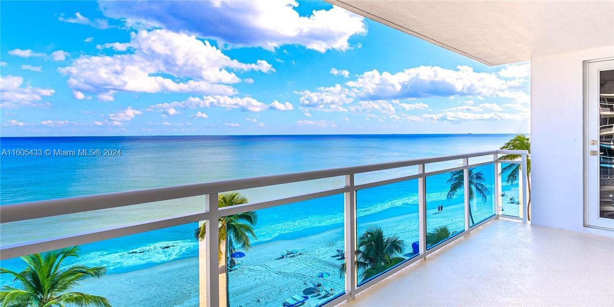 A balcony with a glass railing overlooks a sandy beach and the ocean — FORT LAUDERDALE, FL