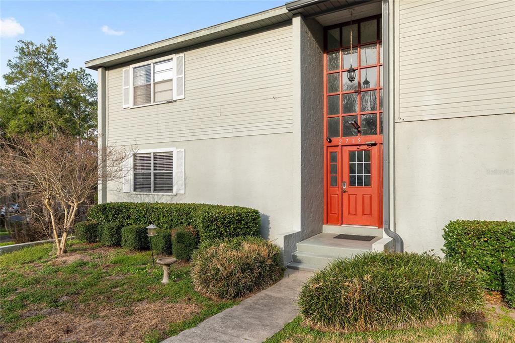 A two-story building exterior features light gray siding, a red front door, and manicured landscaping — 2715 NW 104TH COURT UNIT 1, GAINESVILLE, FL