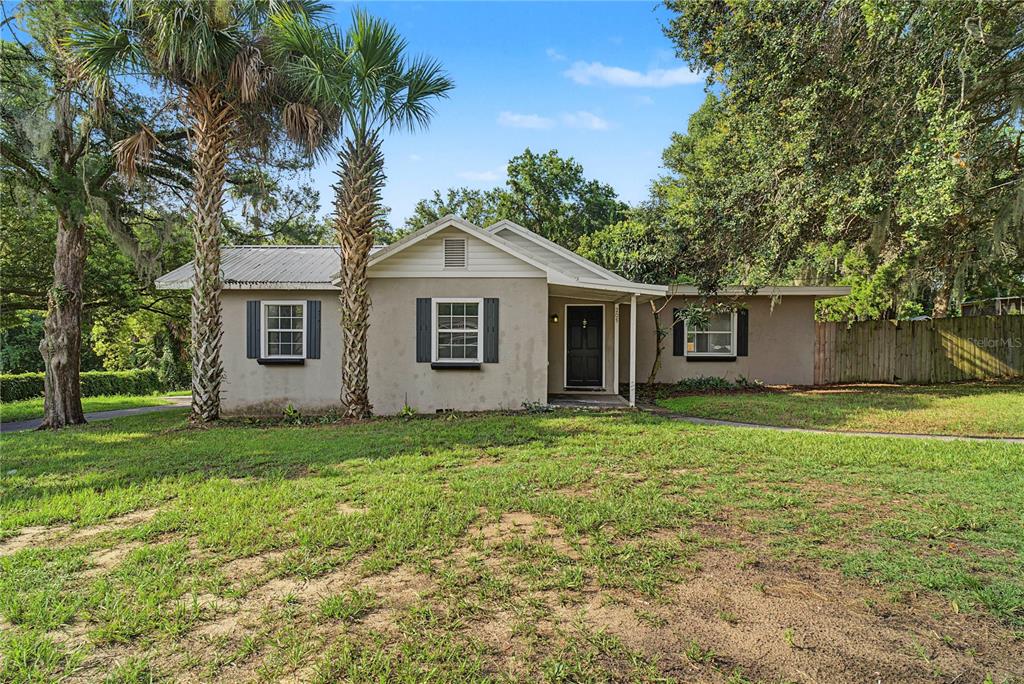 A single-story house with a metal roof, beige stucco exterior, and two palm trees — 205 E FOUNTAIN STREET, FRUITLAND PARK, FL