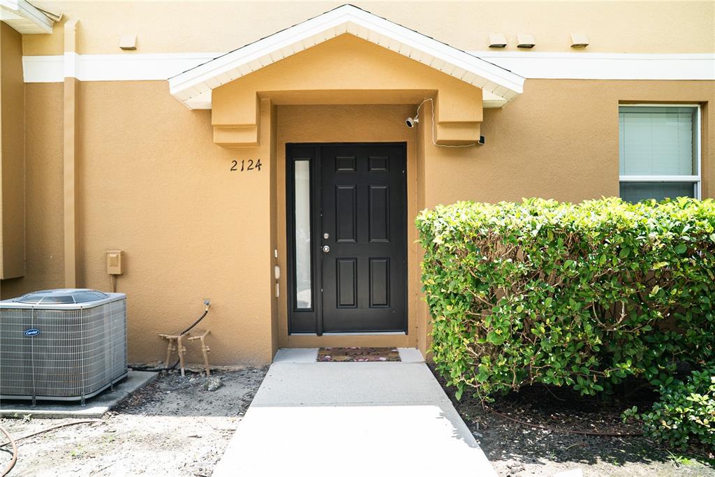 The exterior of a tan building features a black front door, a walkway, and landscaping — 2124 BETSY ROSS LANE, ST CLOUD, FL