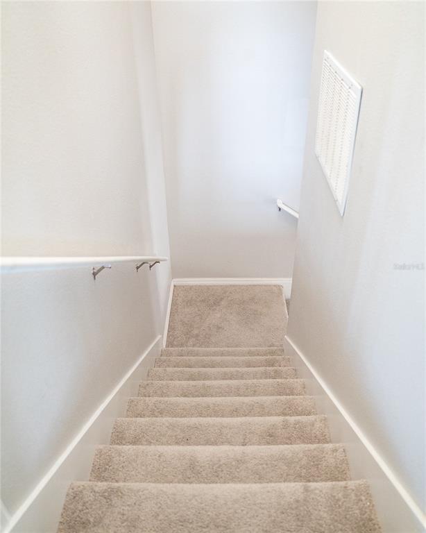A carpeted staircase with white walls and a handrail leads down to a small landing — 2124 BETSY ROSS LANE, ST CLOUD, FL