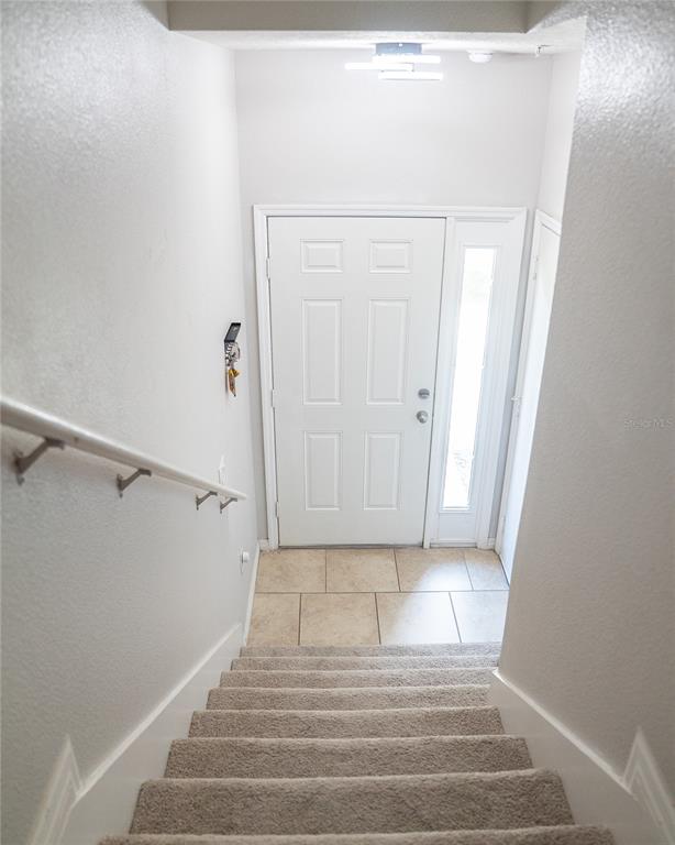 A view looking down carpeted stairs toward a white front door with a side window — 2124 BETSY ROSS LANE, ST CLOUD, FL