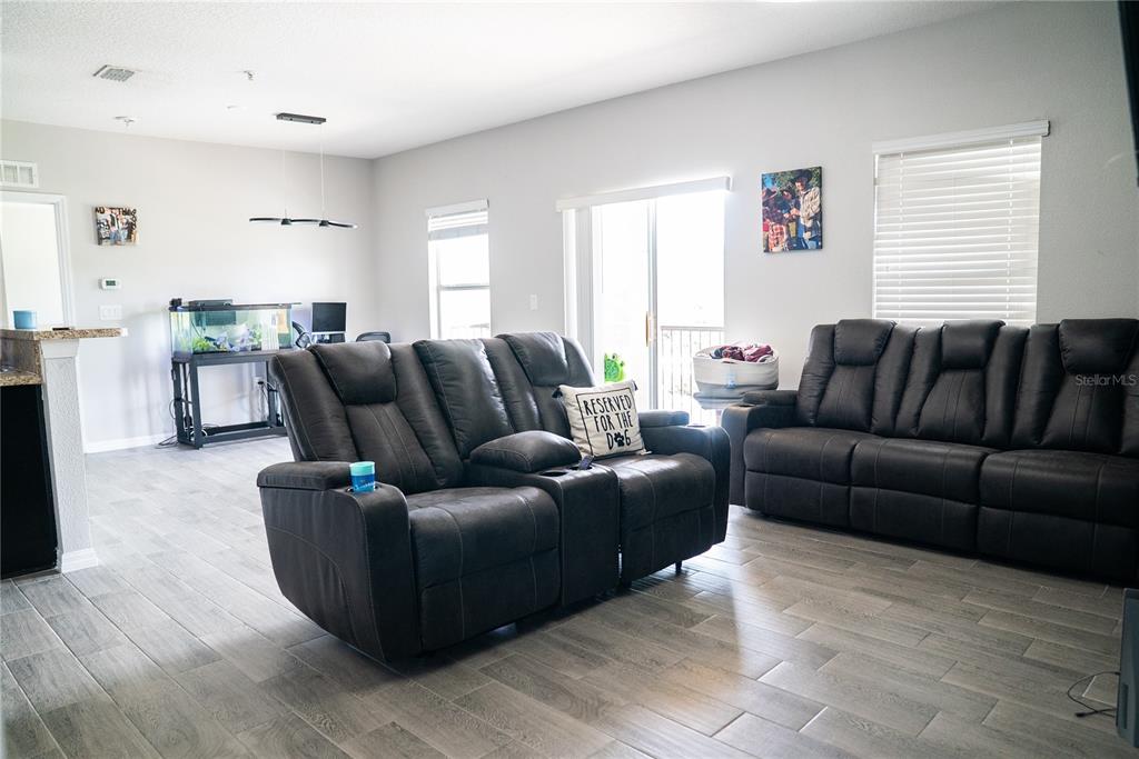 A living room features gray wood-look tile flooring, two dark leather reclining sofas, and an aquarium — 2124 BETSY ROSS LANE, ST CLOUD, FL