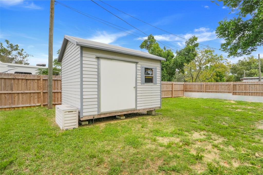 A light gray storage shed with a white door sits on a grassy backyard lot — 3417 CARTER ROAD, HAINES CITY, FL