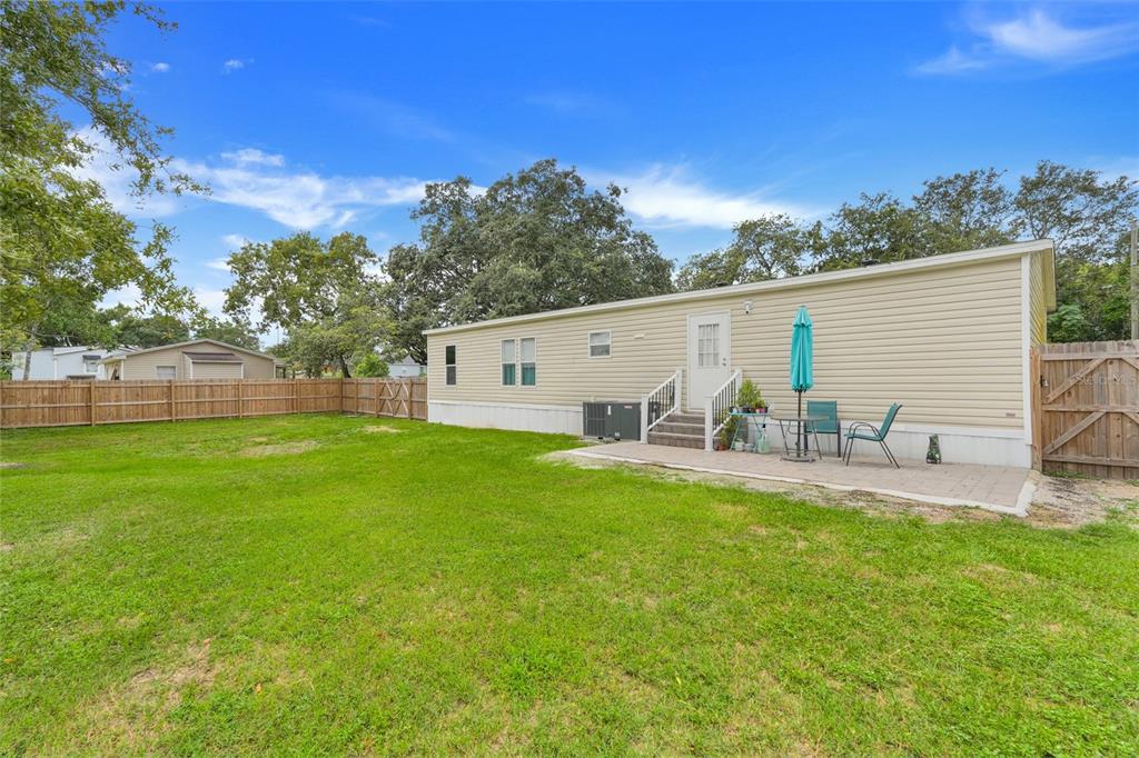 A beige mobile home with a backyard, a paved patio, and a wooden privacy fence — 3417 CARTER ROAD, HAINES CITY, FL