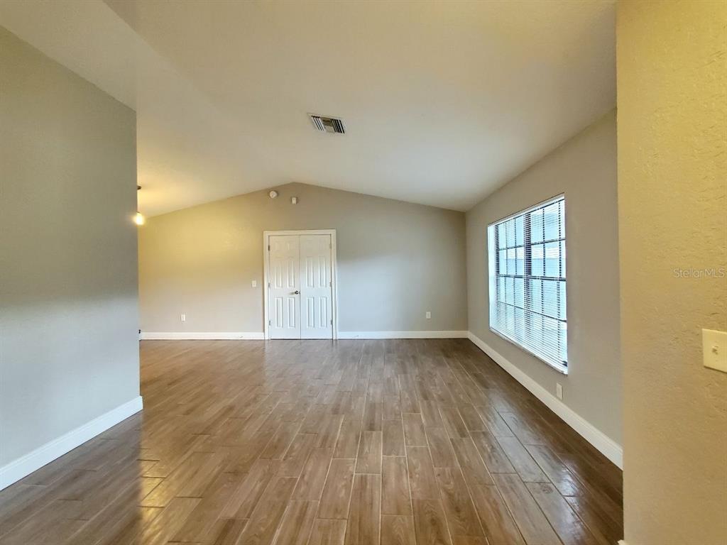 A spacious room features wood-look tile flooring, light gray walls, and a vaulted ceiling — 7432 CANVASBACK DRIVE, NEW PORT RICHEY, FL