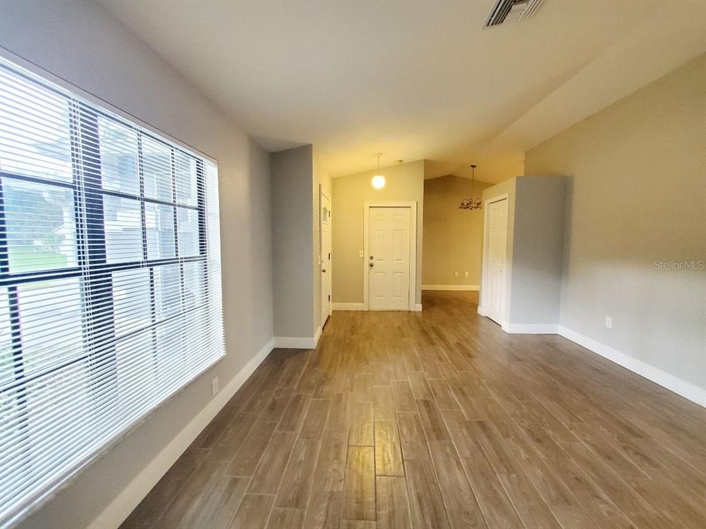 An empty room features wood-look tile flooring, light gray walls, and a large window — 7432 CANVASBACK DRIVE, NEW PORT RICHEY, FL