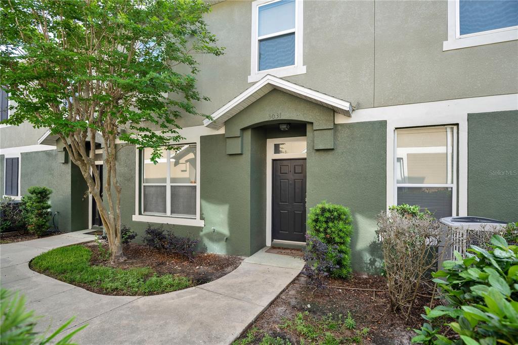The exterior of a two-story townhouse features green stucco walls, a dark front door, and landscaping — 3031 SAN JACINTO CIRCLE UNIT 3031, SANFORD, FL