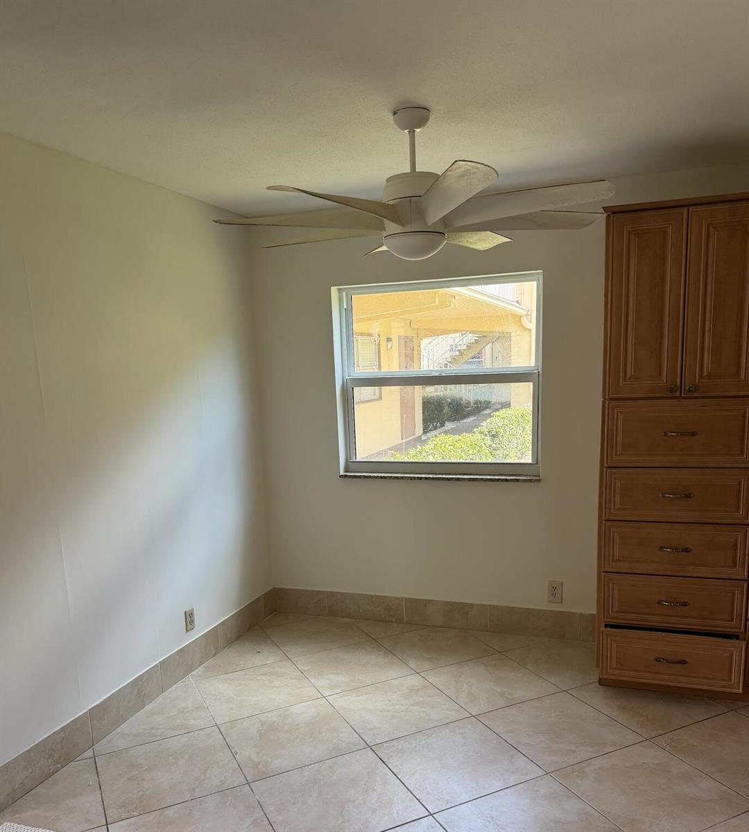 A room with beige tile flooring, a ceiling fan, a window, and a wooden dresser — 157 Saxony D, Delray Beach FL 33446, DELRAY BEACH, FL