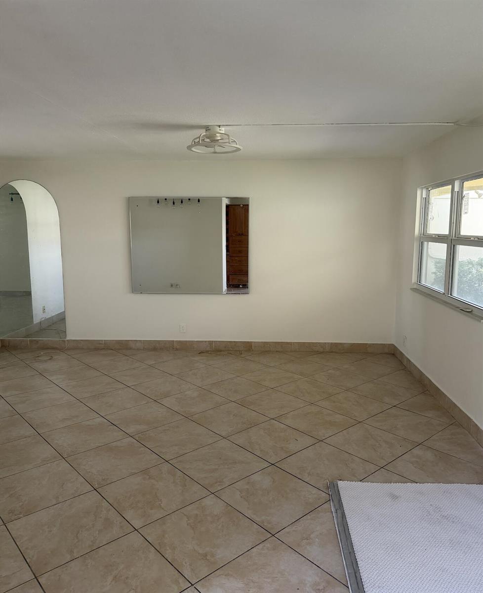 An empty room features beige tile flooring, a large wall mirror, and an arched doorway — 157 Saxony D, Delray Beach FL 33446, DELRAY BEACH, FL