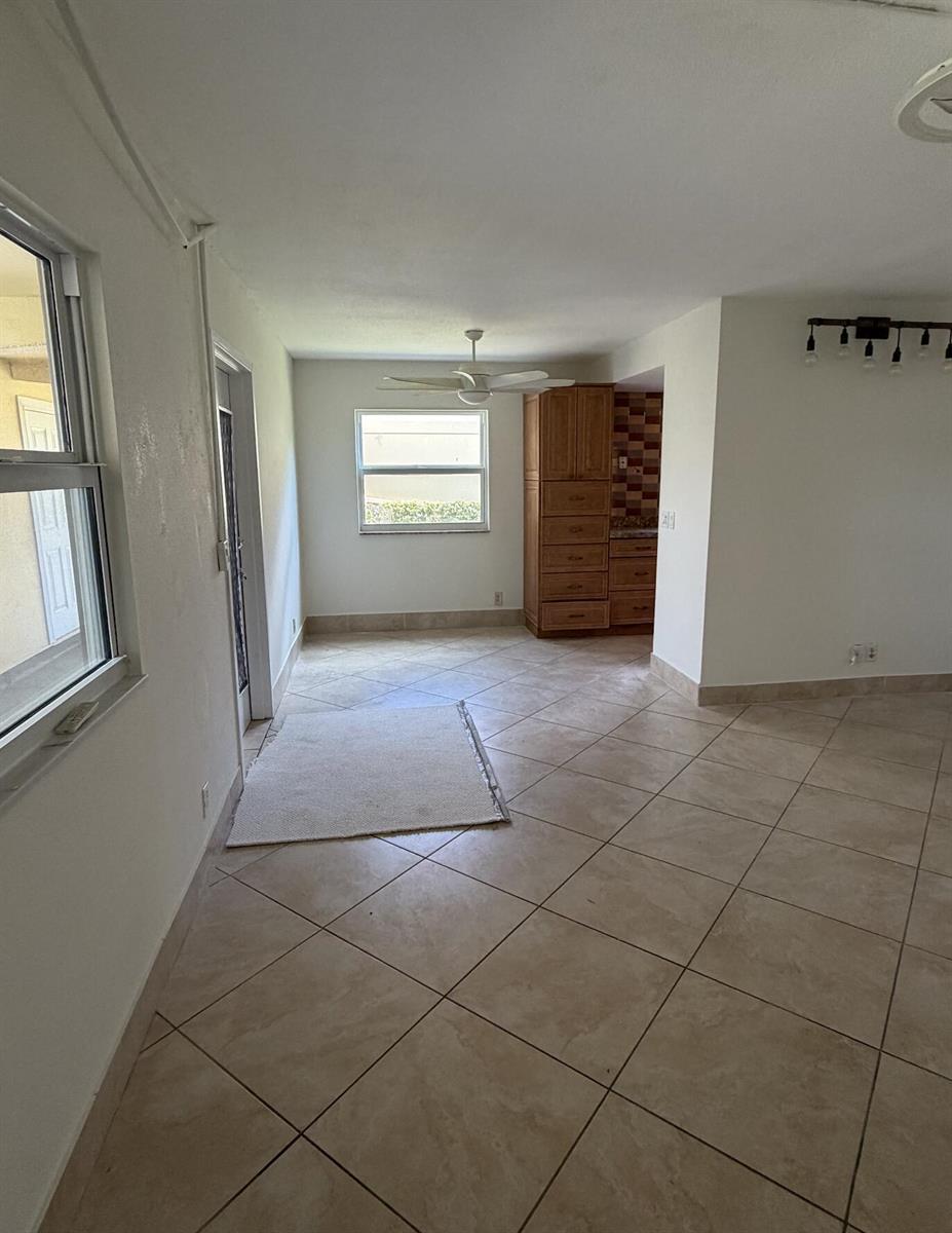 An open-concept room features light-colored tile flooring, a ceiling fan, and a wooden cabinet unit — 157 Saxony D, Delray Beach FL 33446, DELRAY BEACH, FL