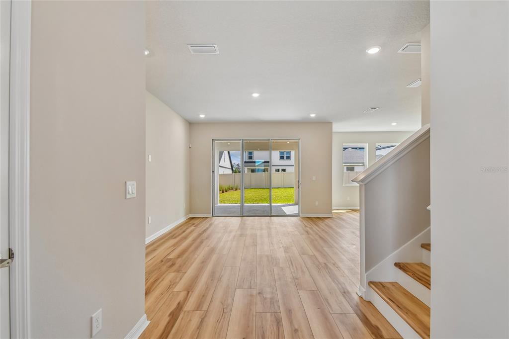 An open-concept living area features light wood-look flooring, a staircase, and sliding glass patio doors — 5921 BRISTLE OAK STREET, MOUNT DORA, FL