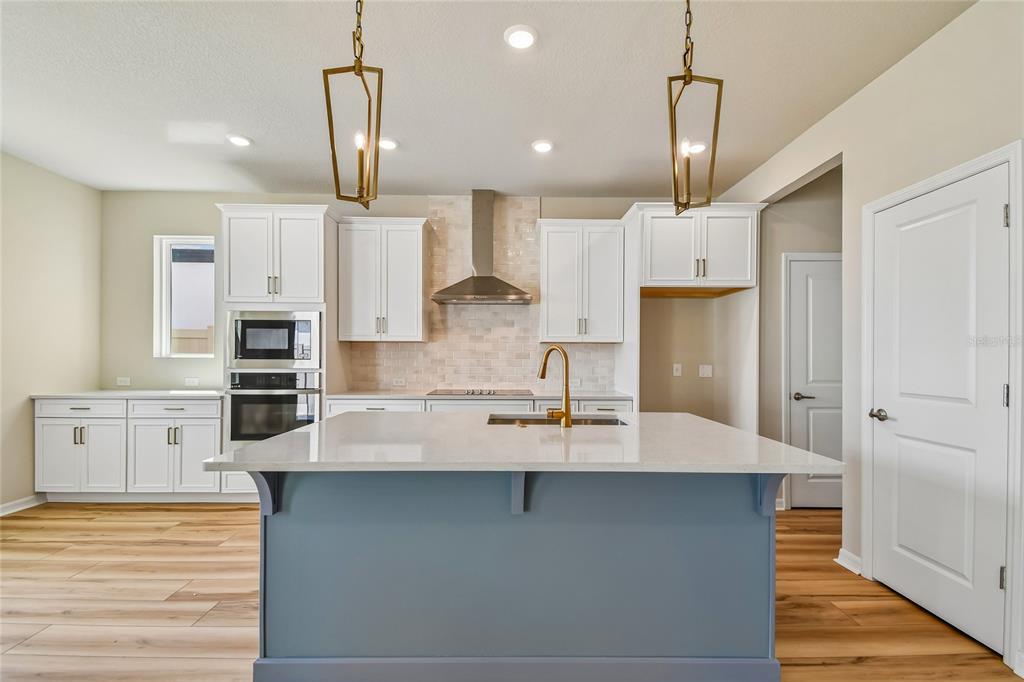 A kitchen features white cabinets, a blue island with a sink, and gold pendant lights — 5921 BRISTLE OAK STREET, MOUNT DORA, FL