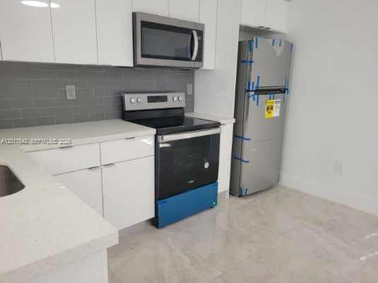 A kitchen features white cabinets, stainless steel appliances, and gray subway tile backsplash — 1725 Calais Dr # 6, Miami Beach FL 33141, MIAMI BEACH, FL
